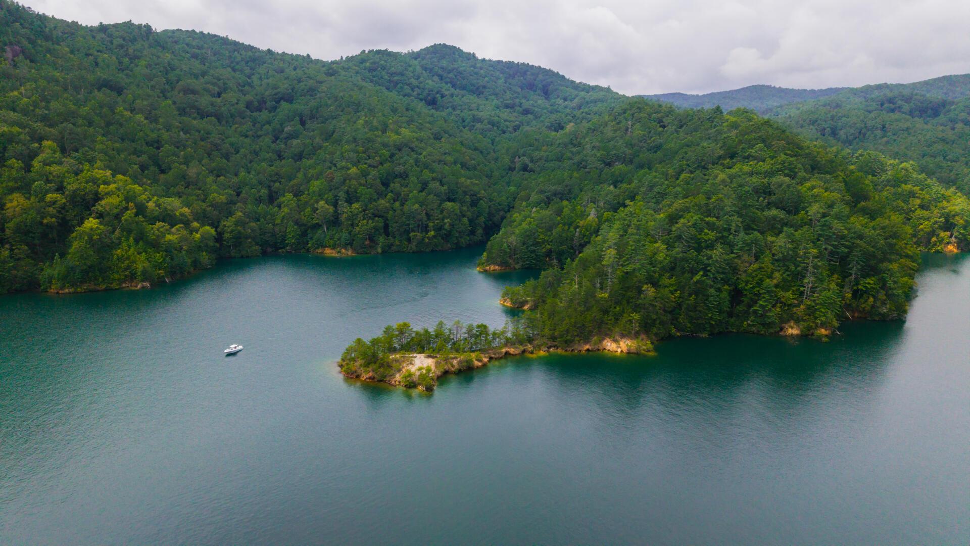 Aerial view of a small boat on a pristine mountain lake surrounded by dense forested shorelines