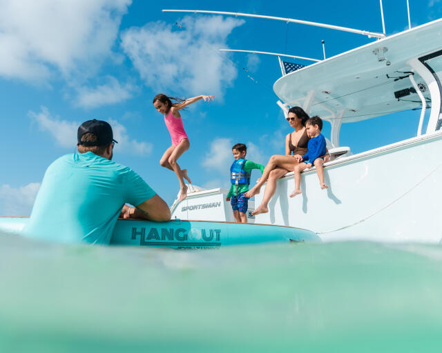Family enjoying a sandbar, with children jumping and swimming off a white center console boat in shallow turquoise water