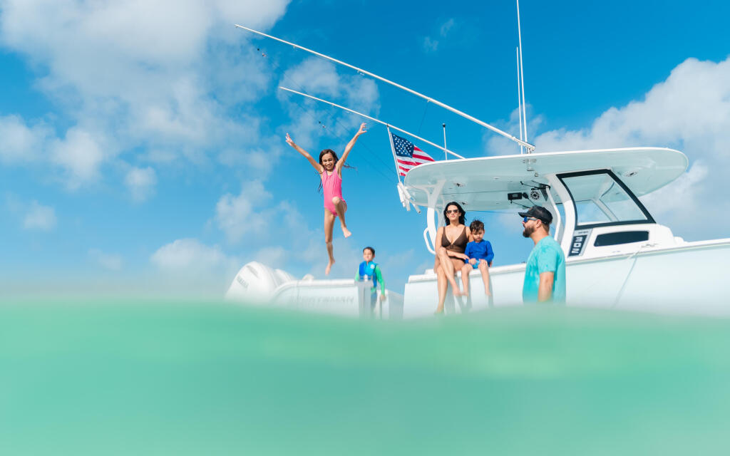 Family swimming and playing in shallow turquoise water next to a white center console boat with an American flag