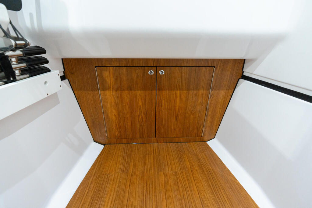Wooden cabinet with chrome handles and white gel-coat interior walls in boat cabin storage area