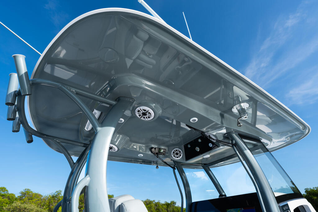Overhead view of boat helm with steering wheel, controls, and windshield under hard-top canopy on clear day
