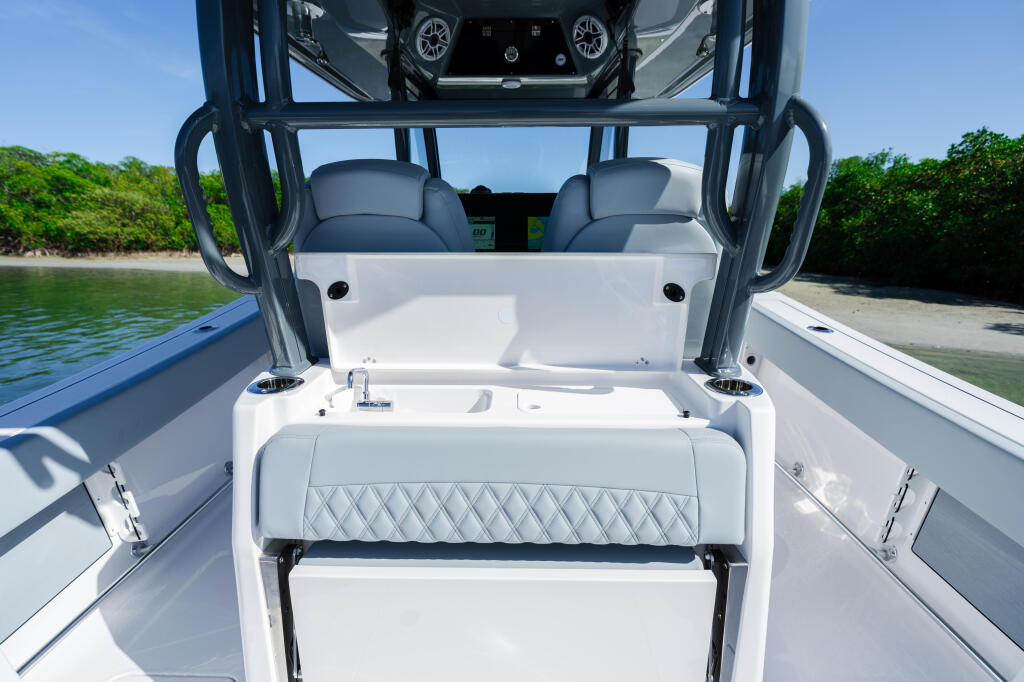 Center console boat with white quilted seating, open cockpit, and hard-top frame overlooking tropical beach and mangroves