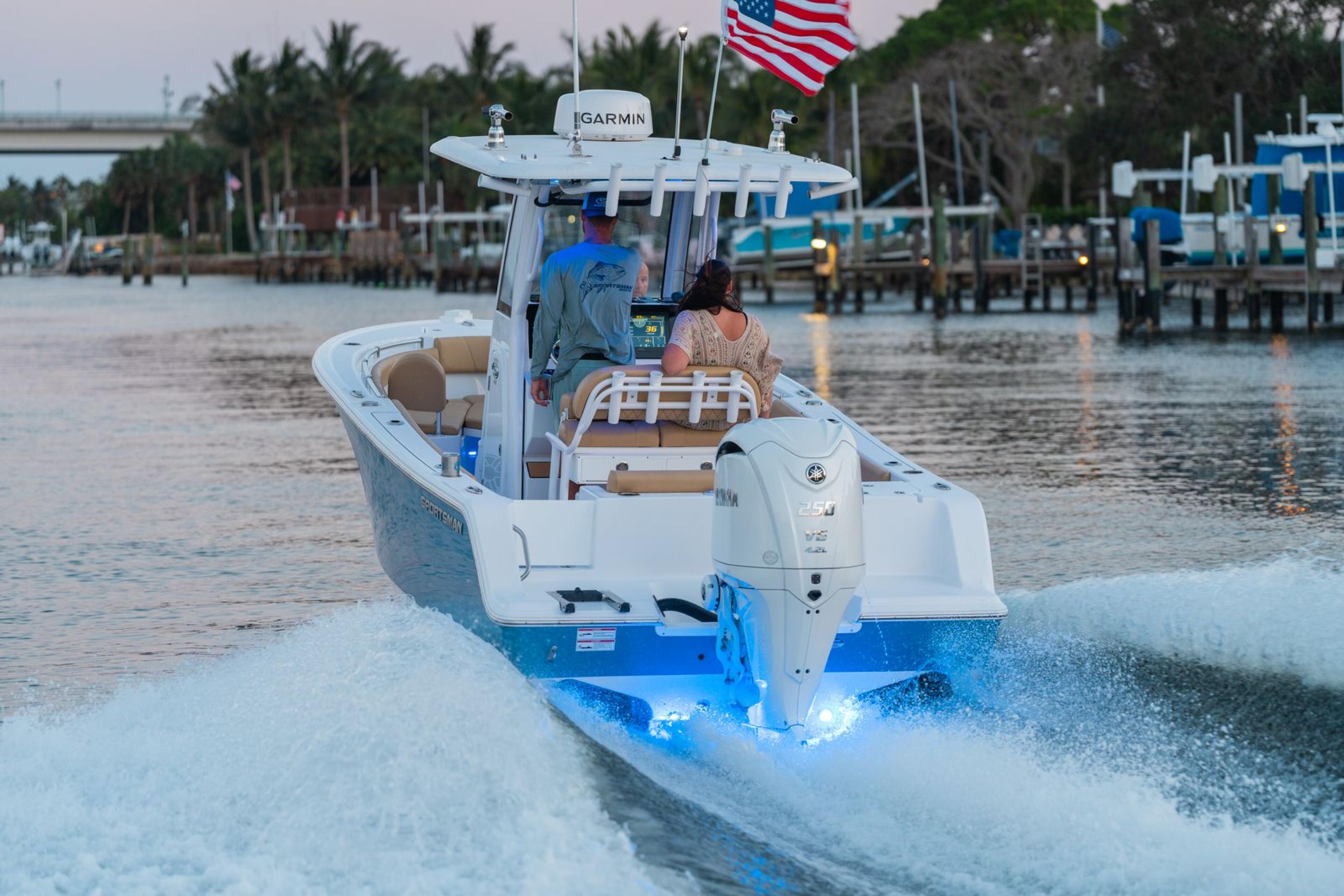 White and blue center console boat running through shallow water near a marina with palm trees and American flag visible