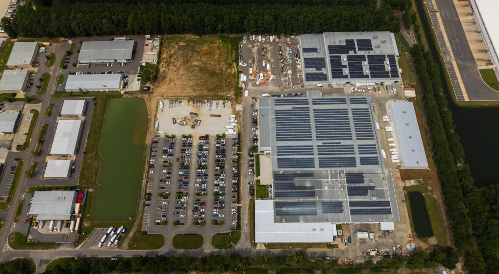 Aerial view of boat manufacturing facility with solar panels, parking lot, and construction areas surrounded by green trees