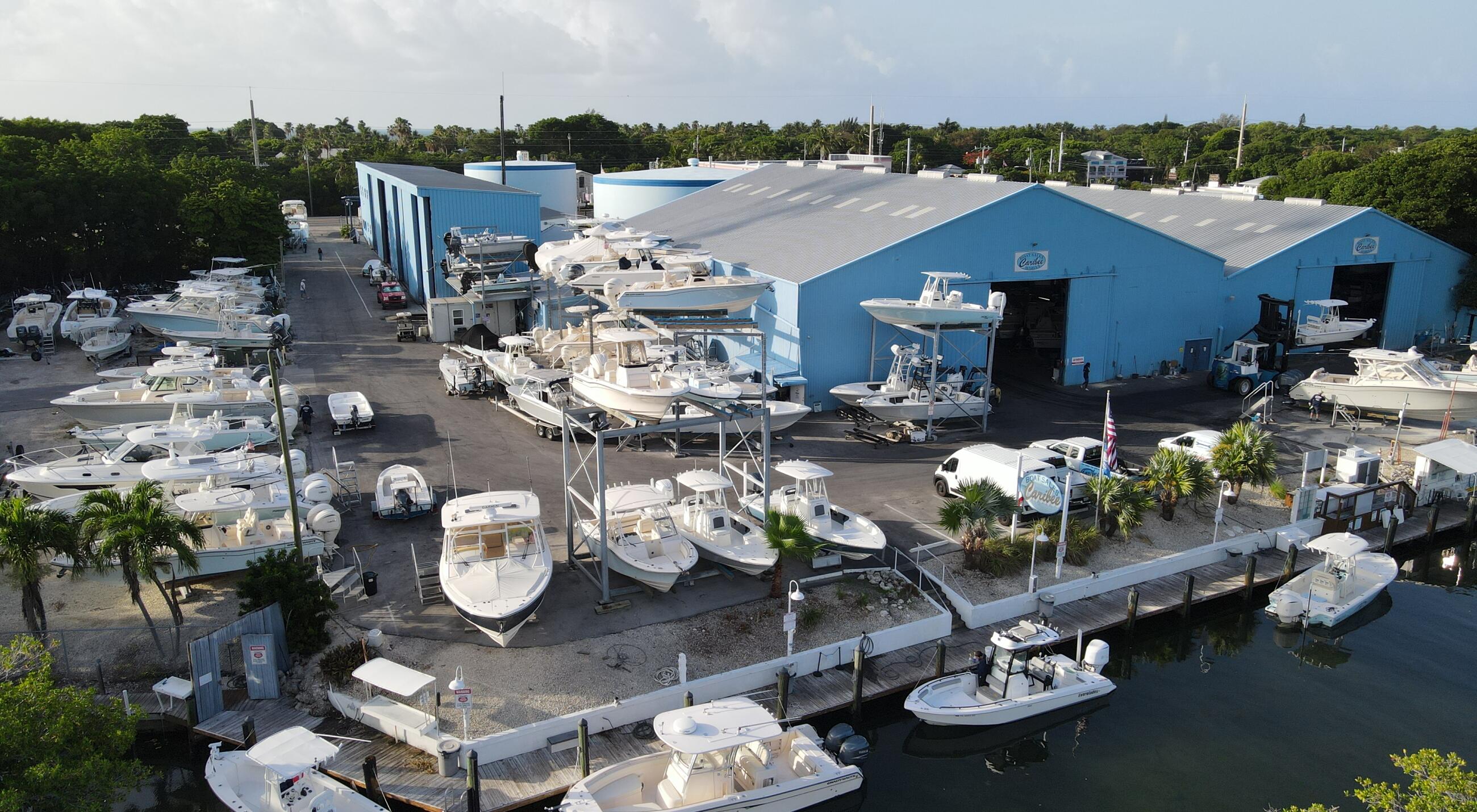 Aerial view of marina with white boats docked beside blue service buildings and repair facilities