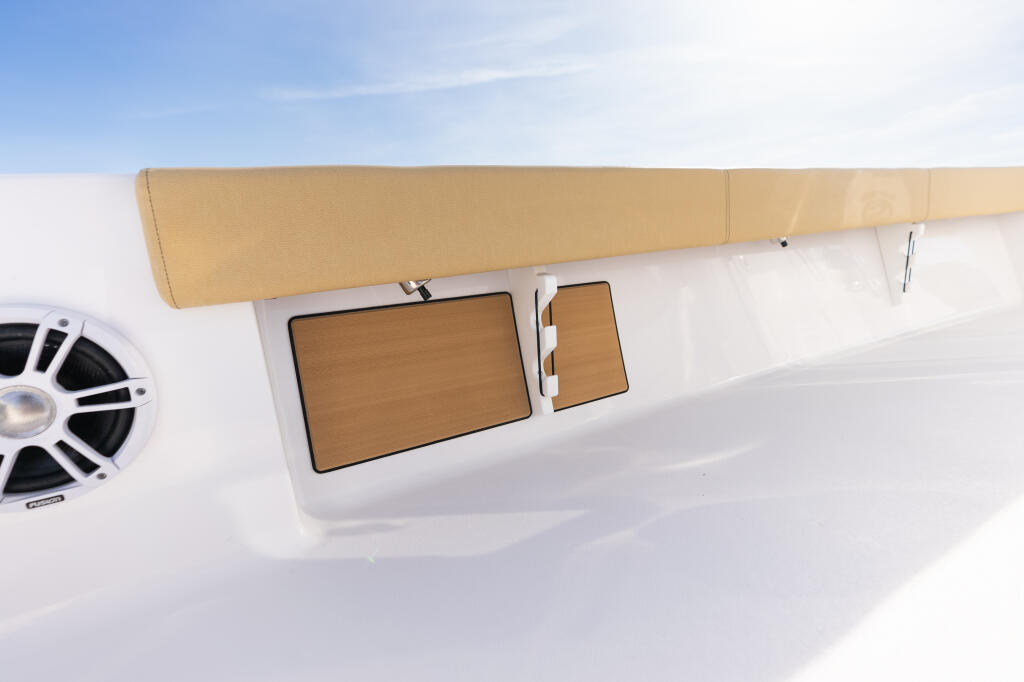 Overhead view of boat's white gunwale with tan cushioned backrest, wooden-trimmed storage compartments, and built-in rod racks