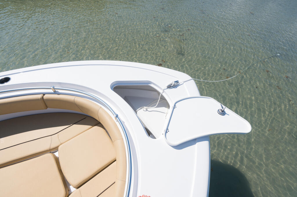 Overhead view of boat's white bow with beige seating and open anchor locker over shallow turquoise water