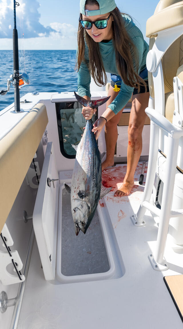 Woman proudly holding a large mackerel on the deck of a center console fishing boat offshore