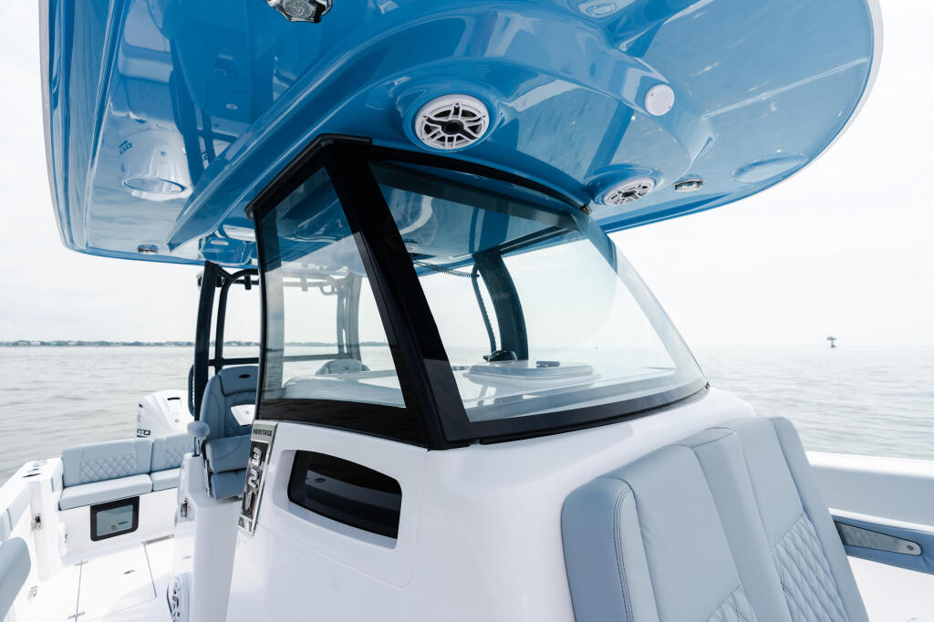 Boat helm with blue hard-top canopy, white seating, and windshield overlooking calm open water