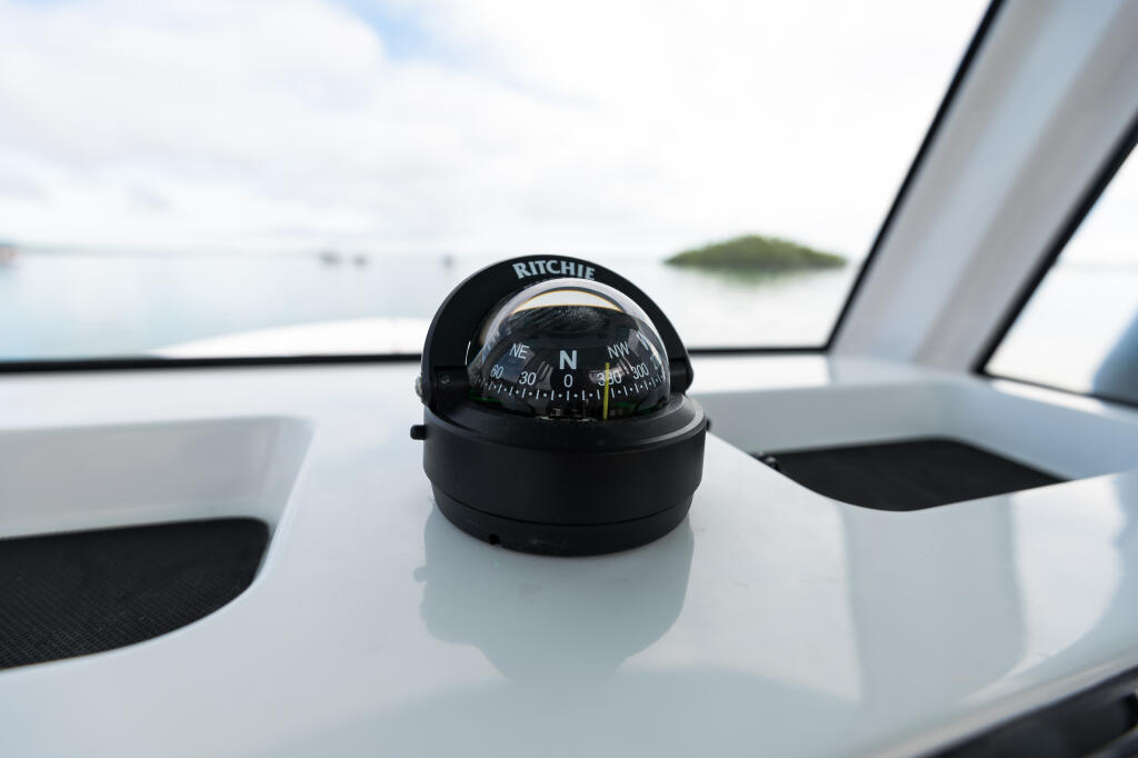Ritchie compass mounted on the helm dashboard of a center console boat with calm waters and islands visible through the windshield