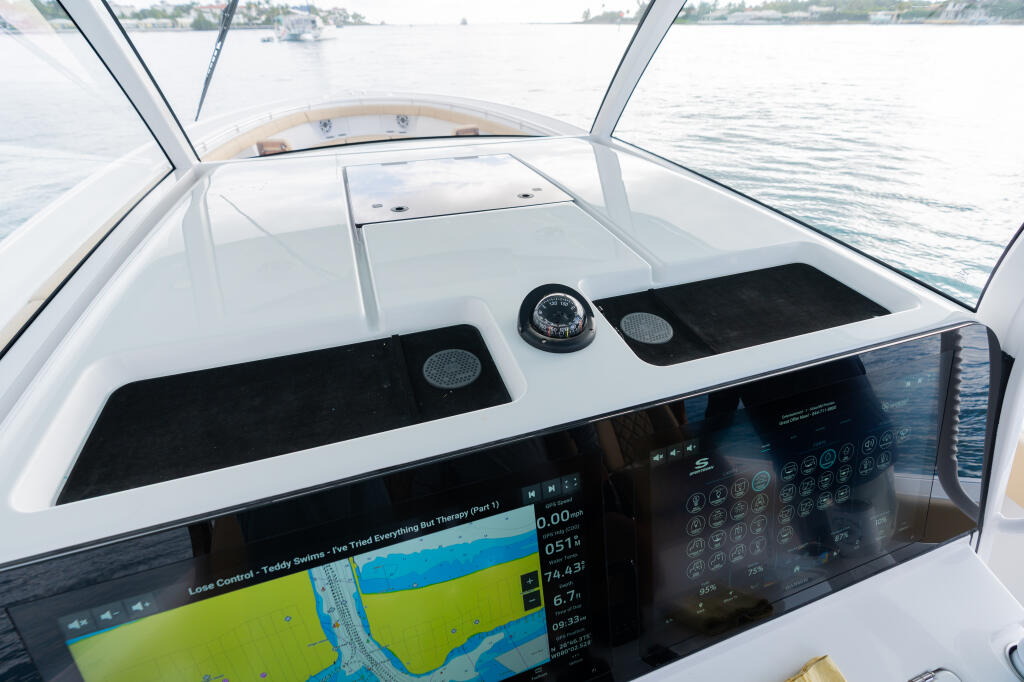 Center console helm with dual monitors displaying navigation and fish finder data, compass, and audio speakers visible through windshield