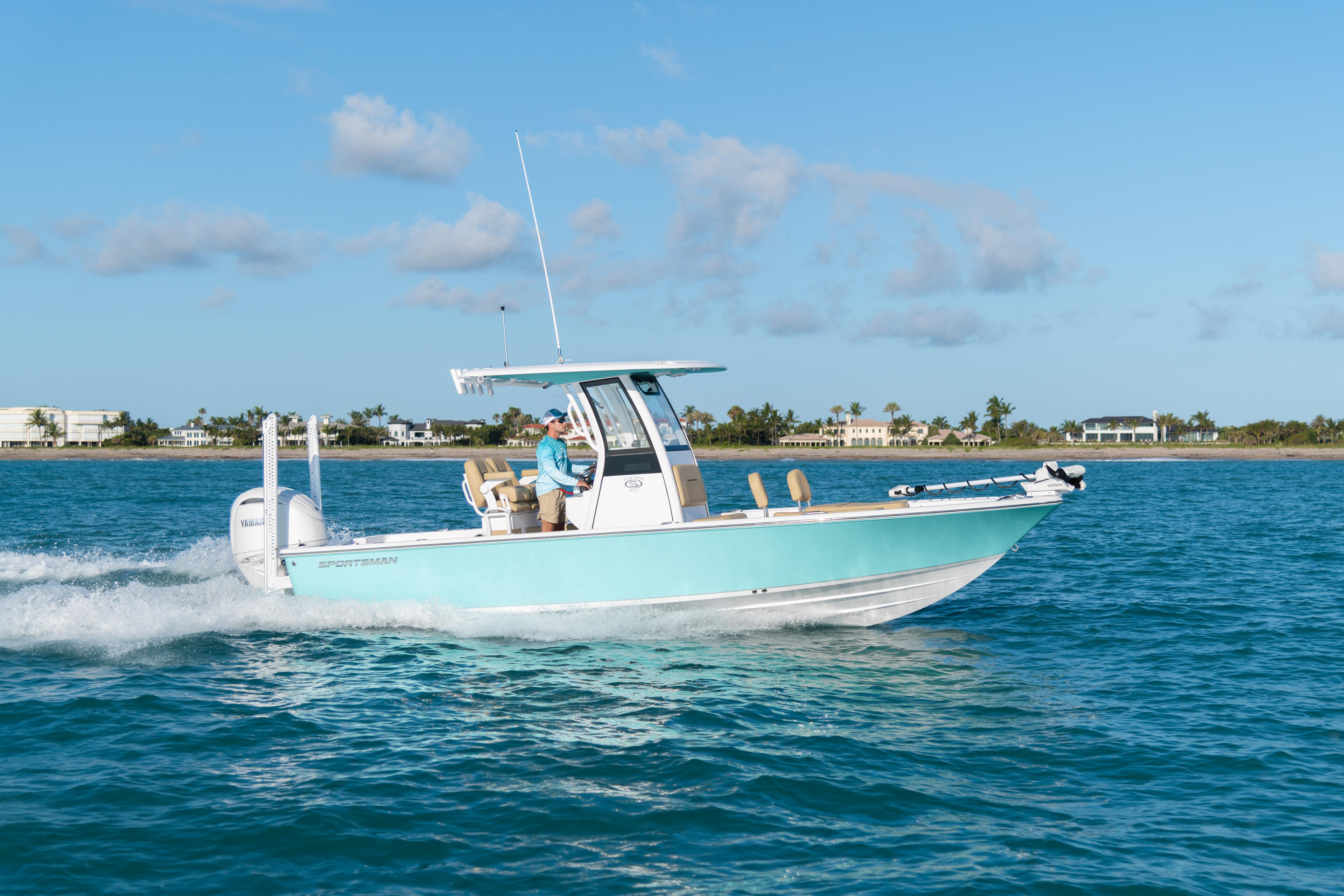 Turquoise and white center console boat running through clear blue water offshore with coastal homes visible in the distance