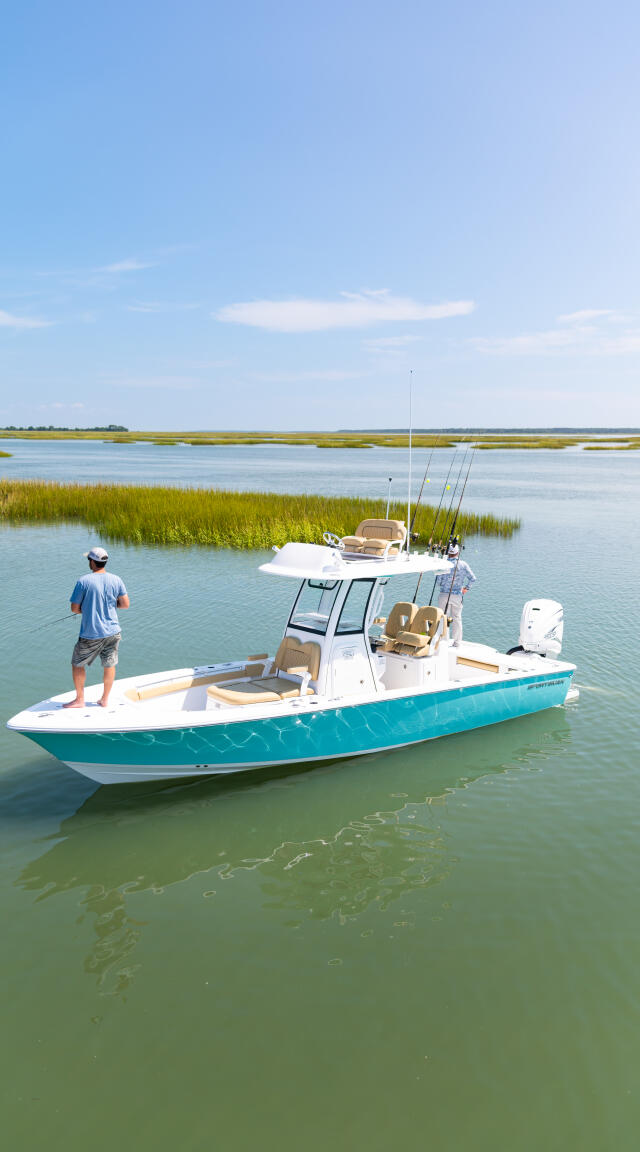 Turquoise and white fishing boat anchored in shallow marsh waters with angler standing on bow