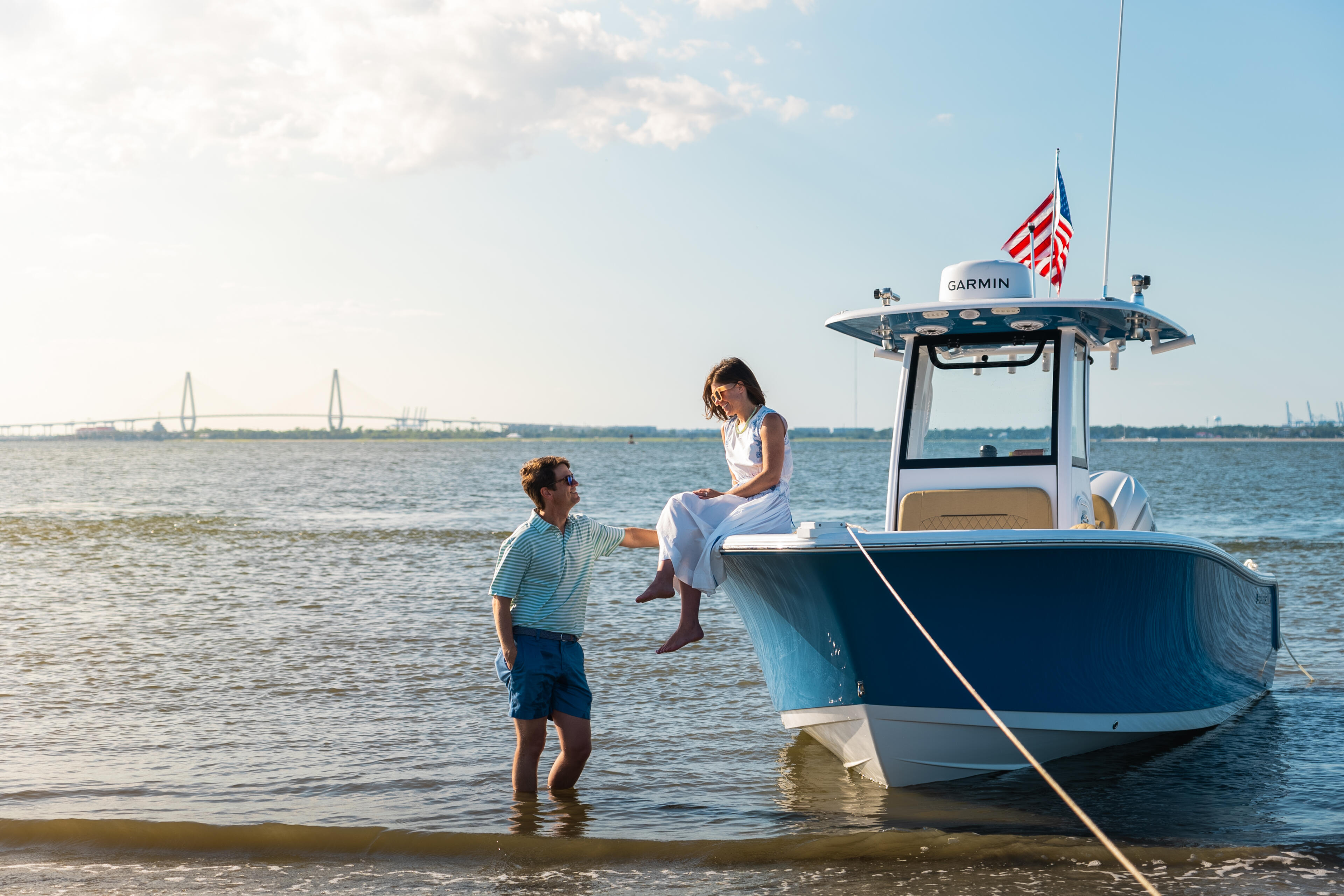 Woman and boy wade in shallow water next to a docked center console boat with Garmin electronics and American flag