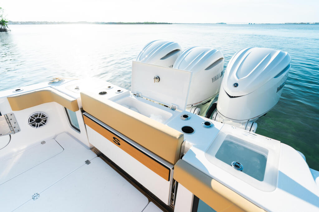 Triple outboard engines mounted on the transom of a white and tan center console boat at a calm marina