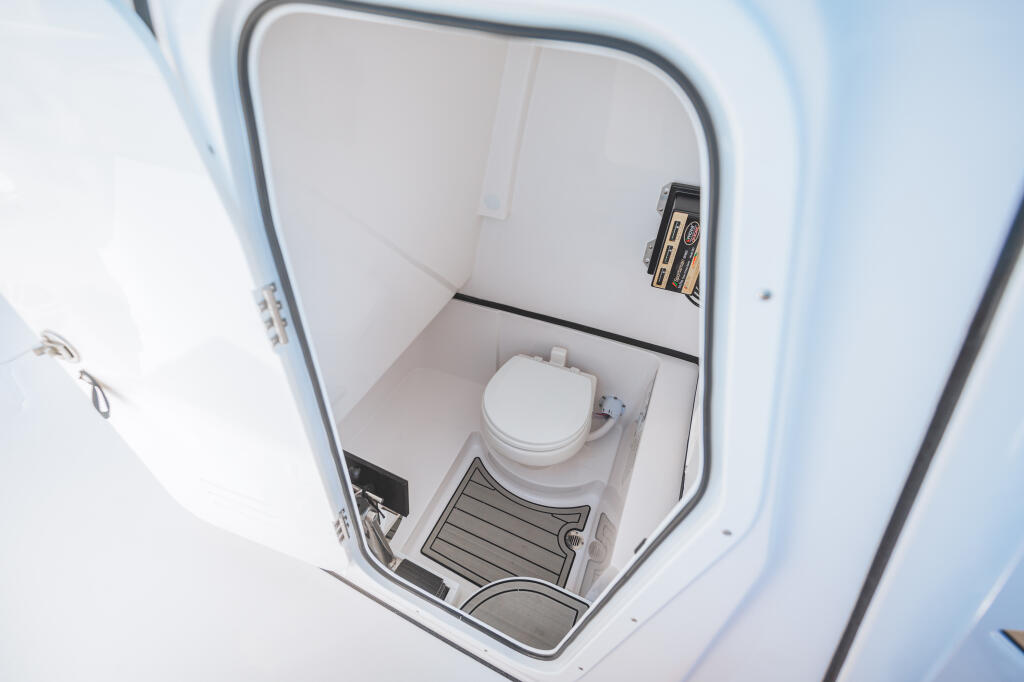 Compact boat head with white toilet, storage compartment, and mirror in white fiberglass enclosure