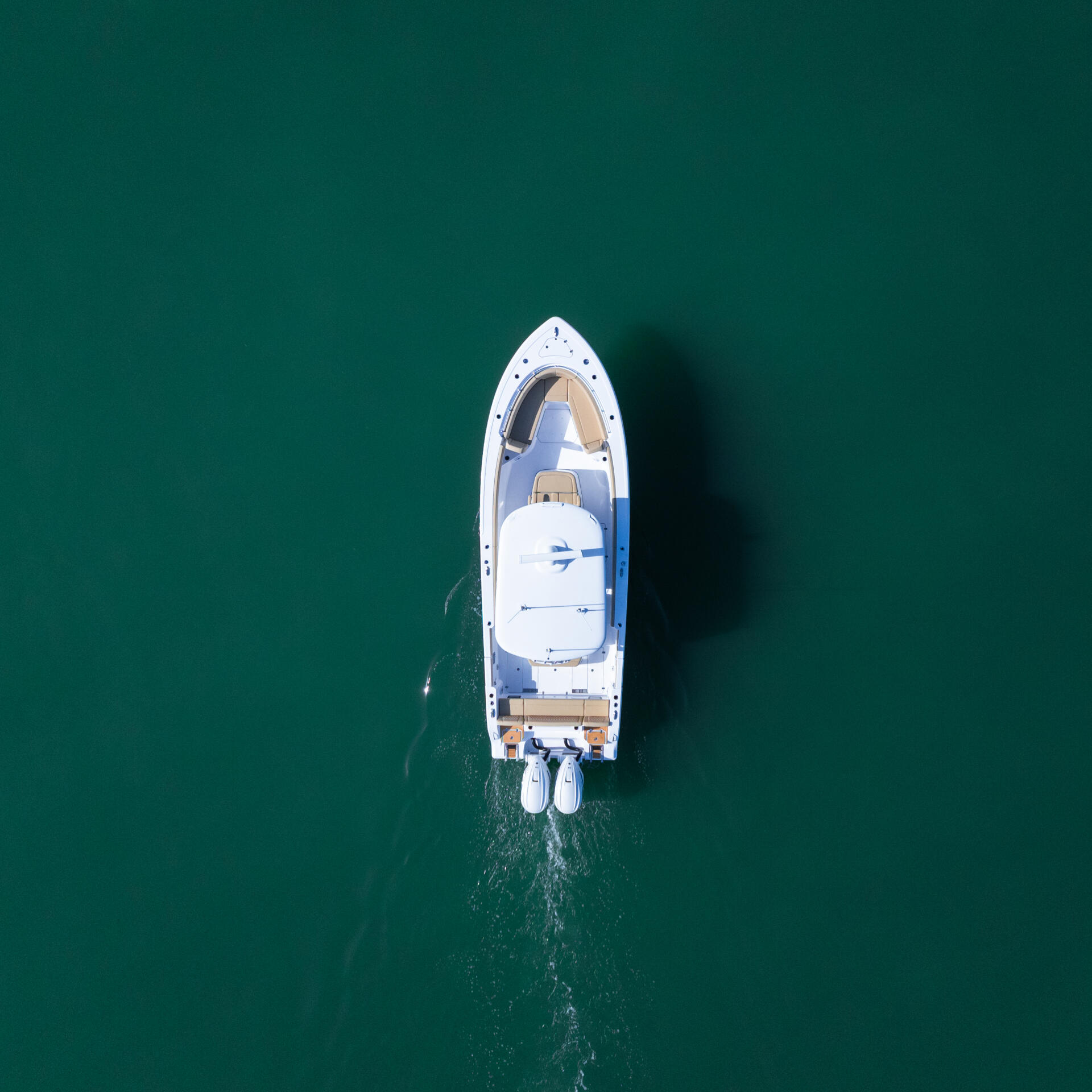 White sport fishing boat anchored in shallow turquoise water, shot from directly above