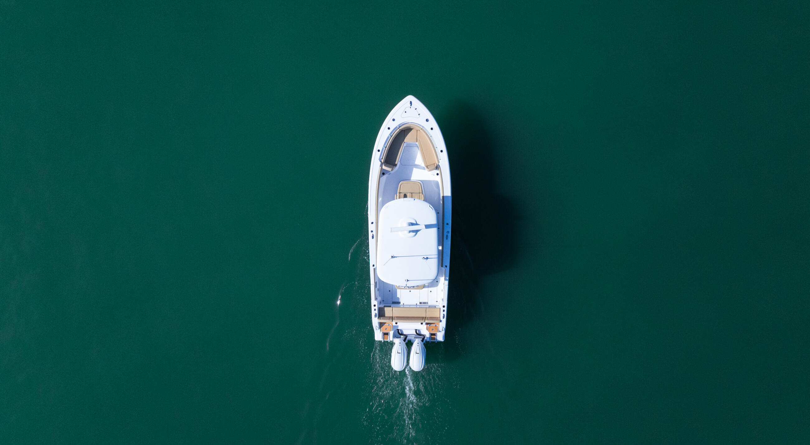 White sport fishing boat anchored in shallow turquoise water, shot from directly above