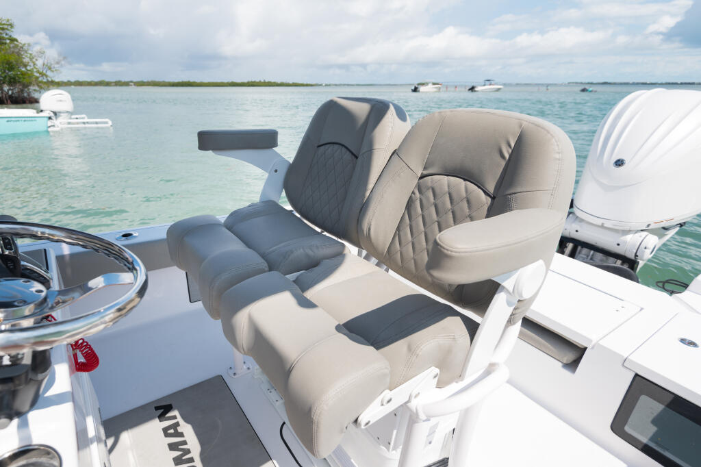 Dual captain chairs with gray and tan upholstery and flip-up bolsters on a center console boat anchored in clear shallow water