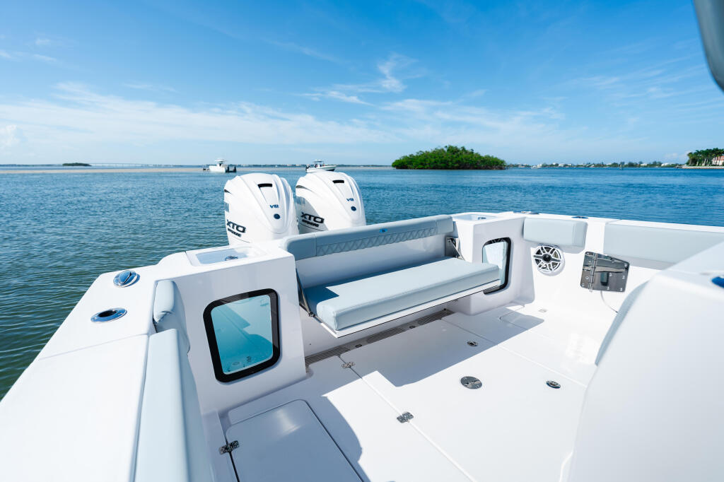 Twin outboard engines and open cockpit seating on a white center console boat anchored in clear blue water