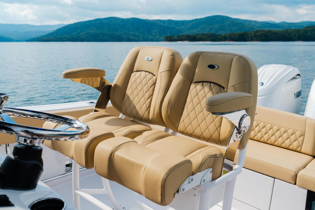 Tan quilted seating on a boat helm with mountain lake backdrop and forested shoreline