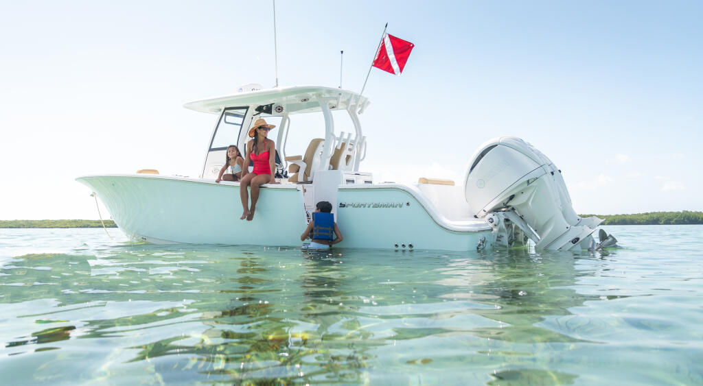 Family enjoying shallow turquoise waters at a sandbar with a red dive flag flying from the boat