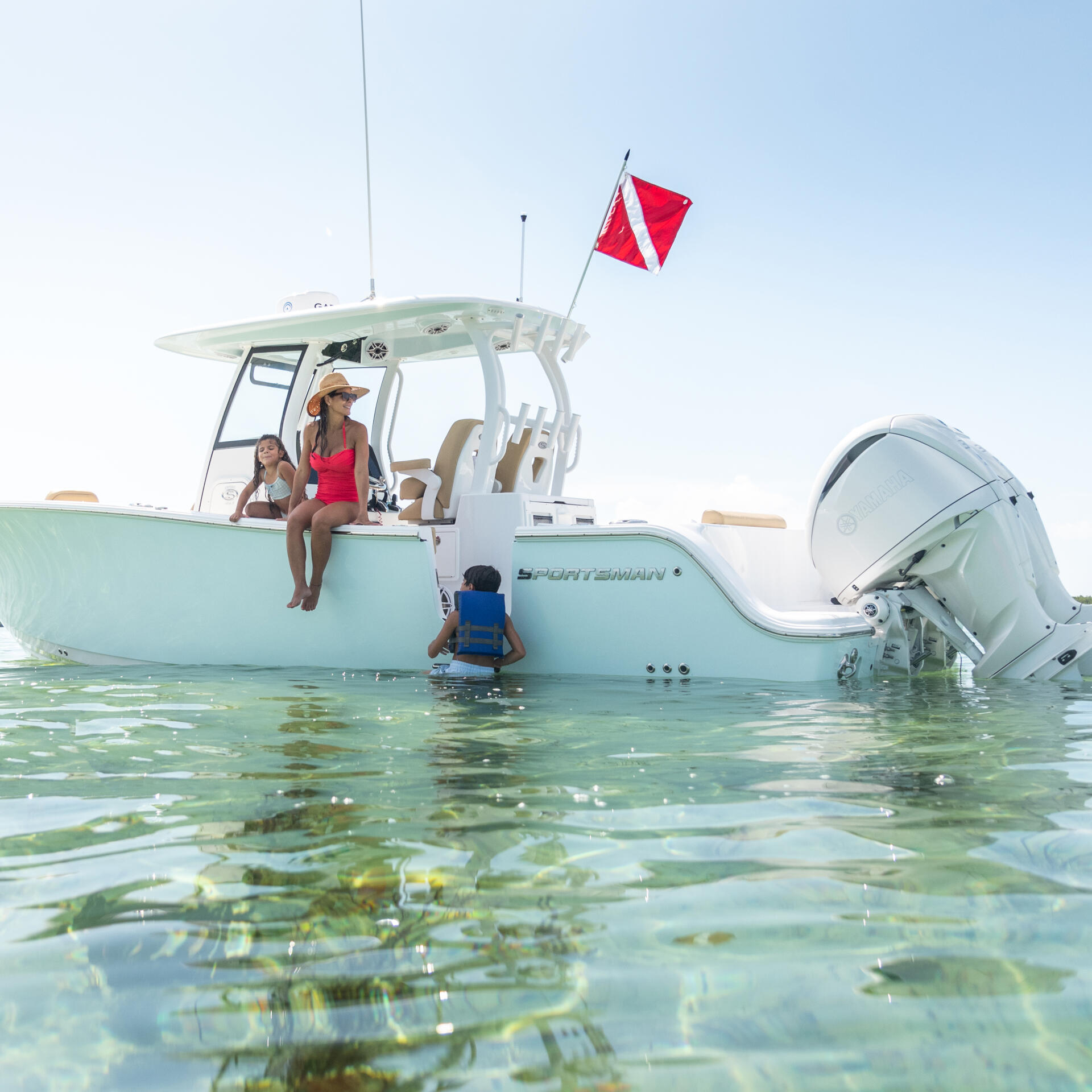 Family enjoying shallow turquoise waters at a sandbar with a red dive flag flying from the boat