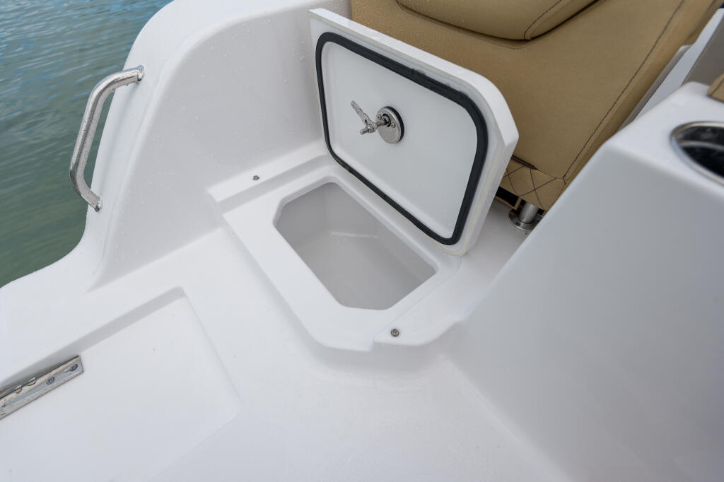 Open cooler with latch and drainplug built into boat deck next to tan seating