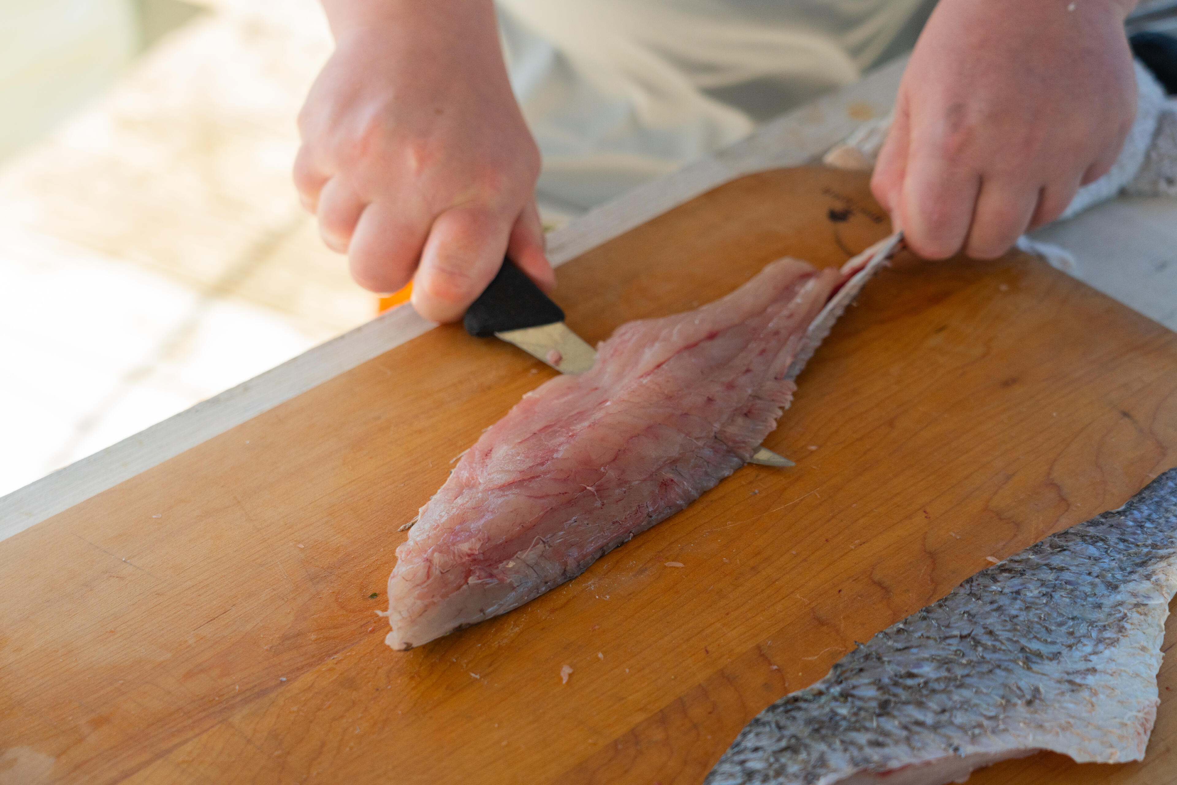 Hands fileting a fresh redfish on a wooden cutting board with a knife