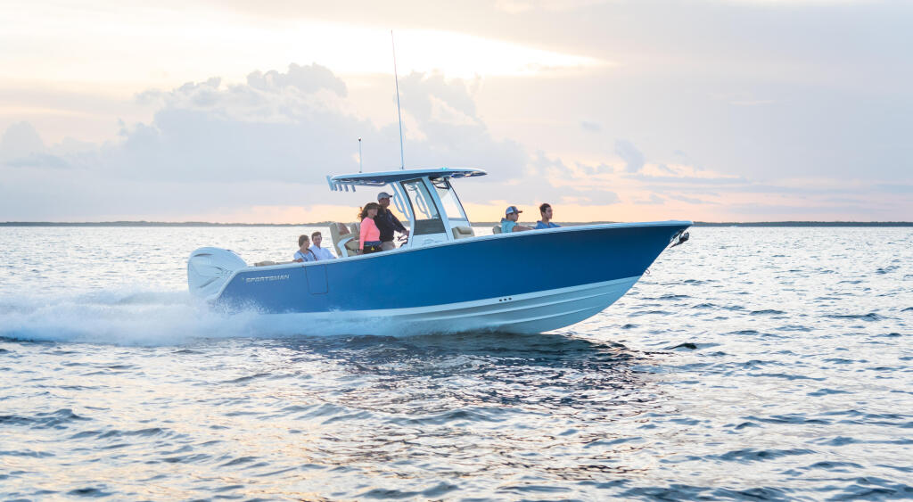 Family group riding a blue center console boat through shallow water near a sandy beach at sunrise