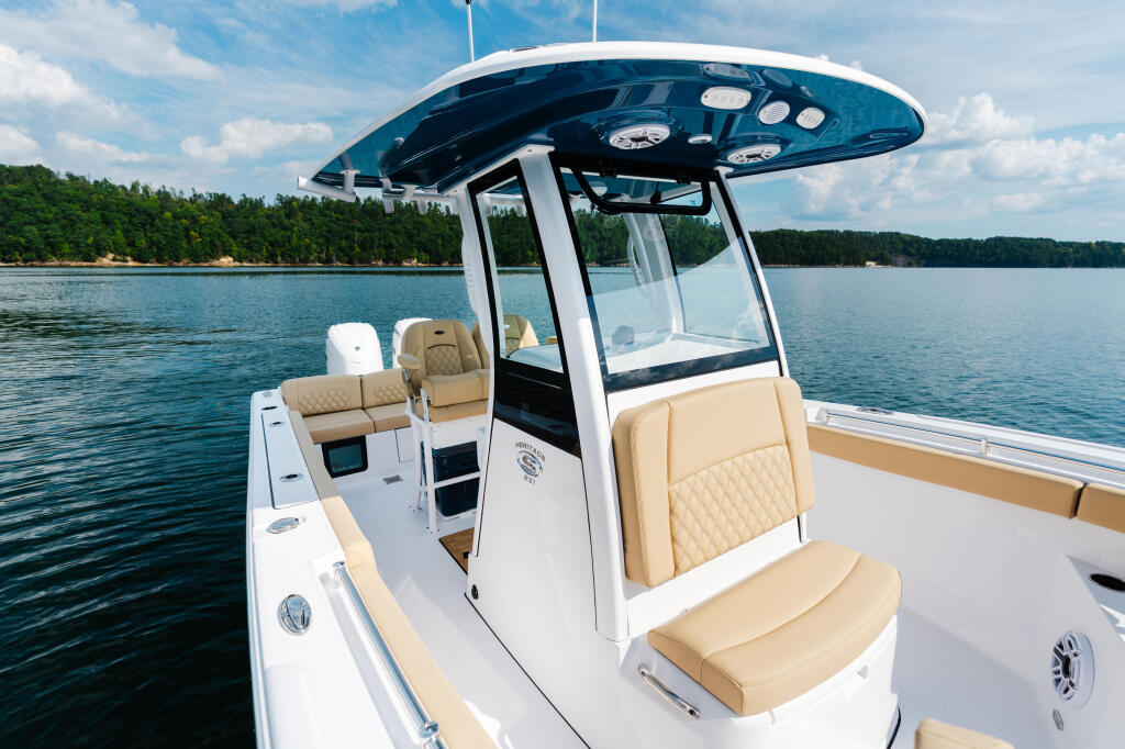 White boat with cream-colored quilted seating and hard-top canopy docked on a calm lake surrounded by forested shoreline