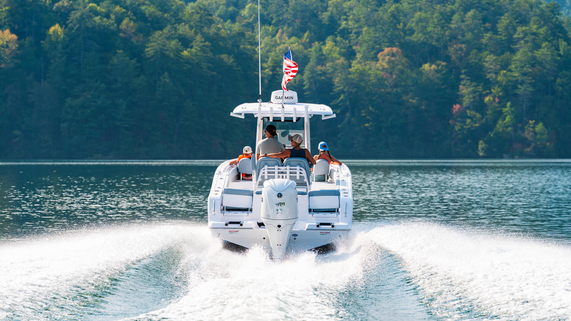 White center console boat running through waves on a forested lake with American flag flying from hardtop