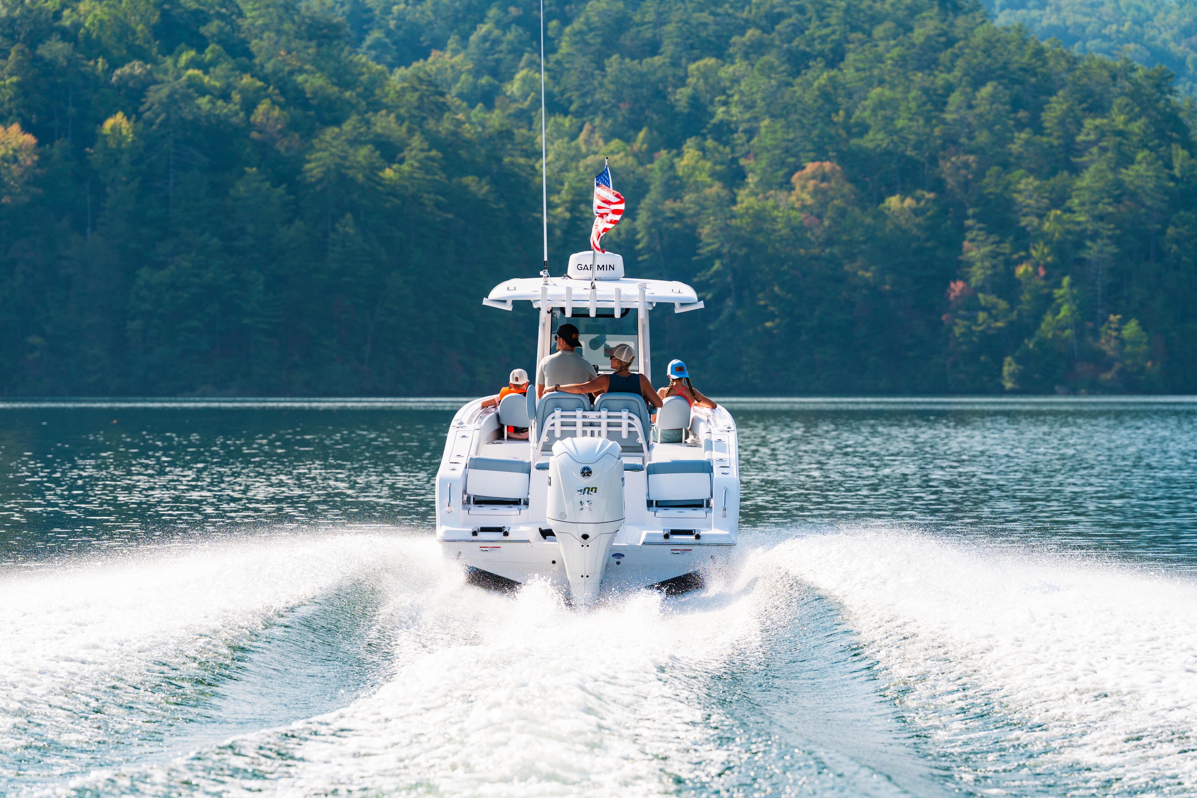 White center console boat running through waves on a forested lake with American flag flying from hardtop