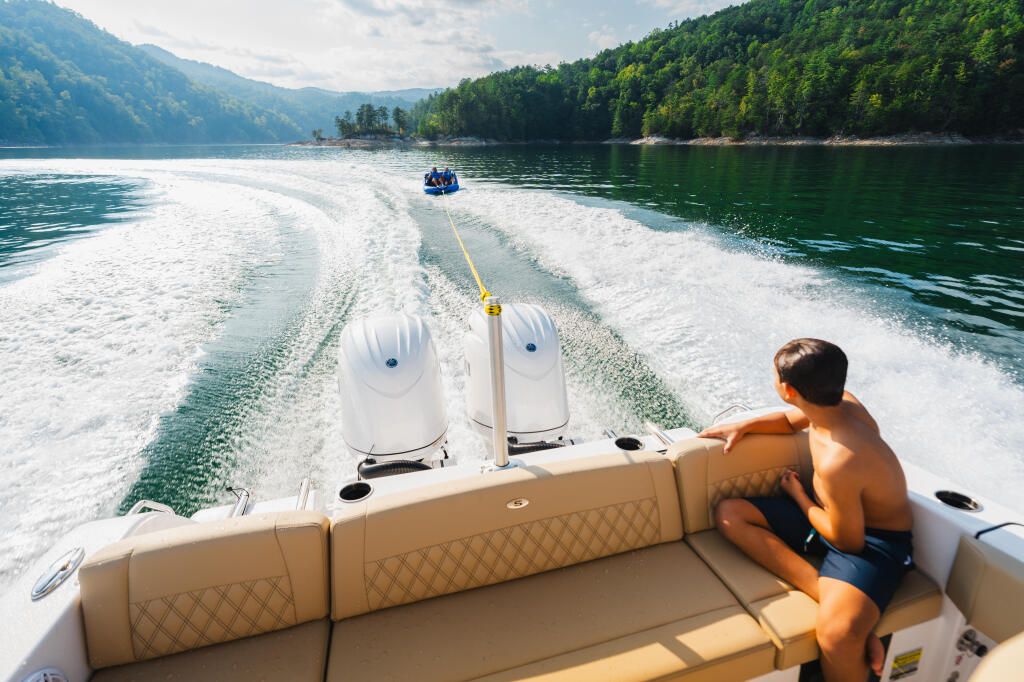 Person towing a tube behind a boat on a mountain lake with forested shores