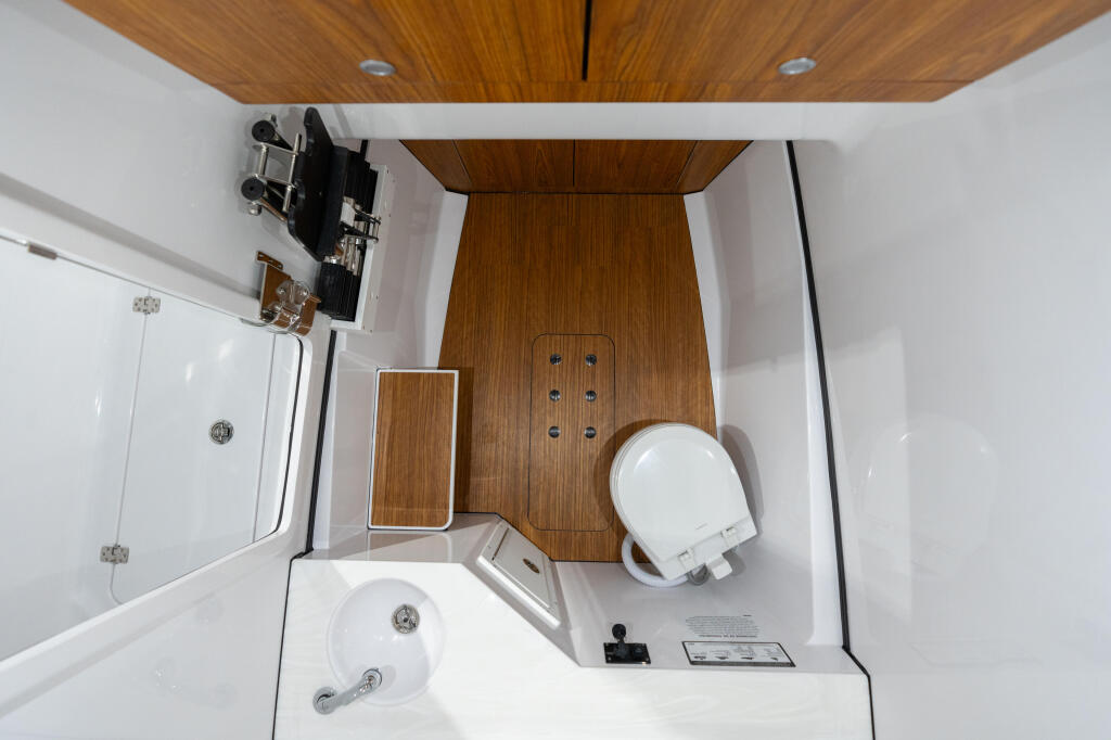 Overhead view of boat cabin bathroom with teak wood ceiling, white fixtures, shower enclosure, and mounted TV