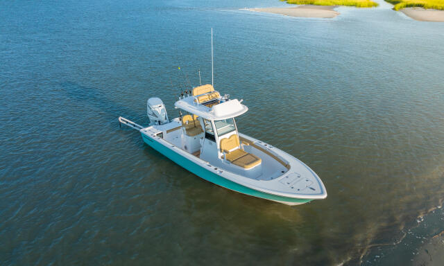 Aerial view of a white and turquoise center console fishing boat anchored in shallow coastal waters near salt marshes