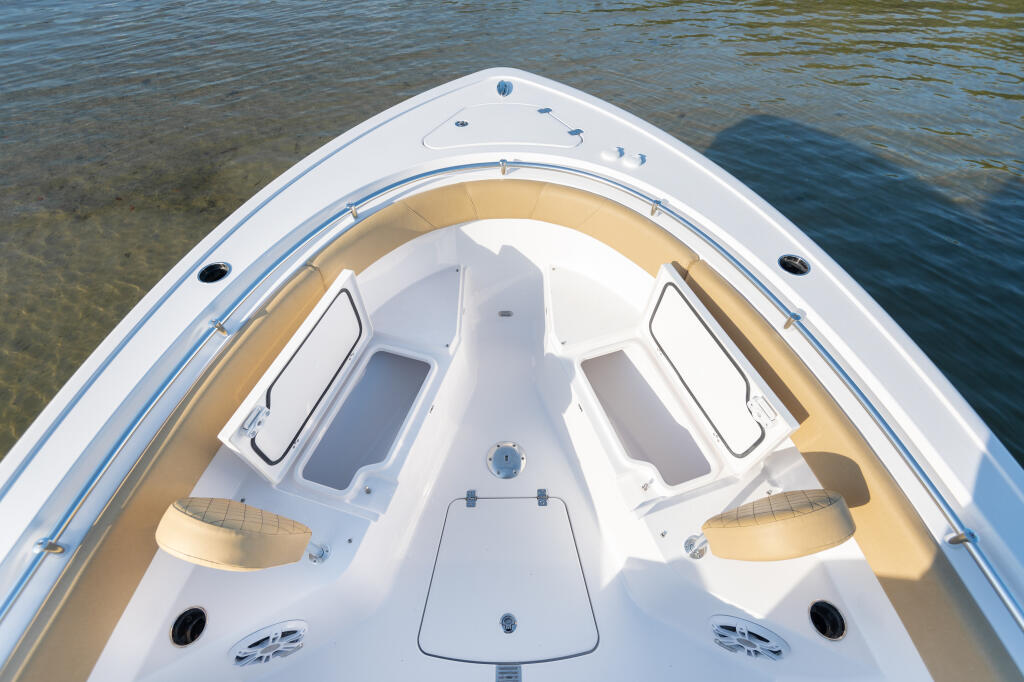 Aerial view of a center console boat's bow featuring tan cushioned seating, white cabin structure, and storage compartments
