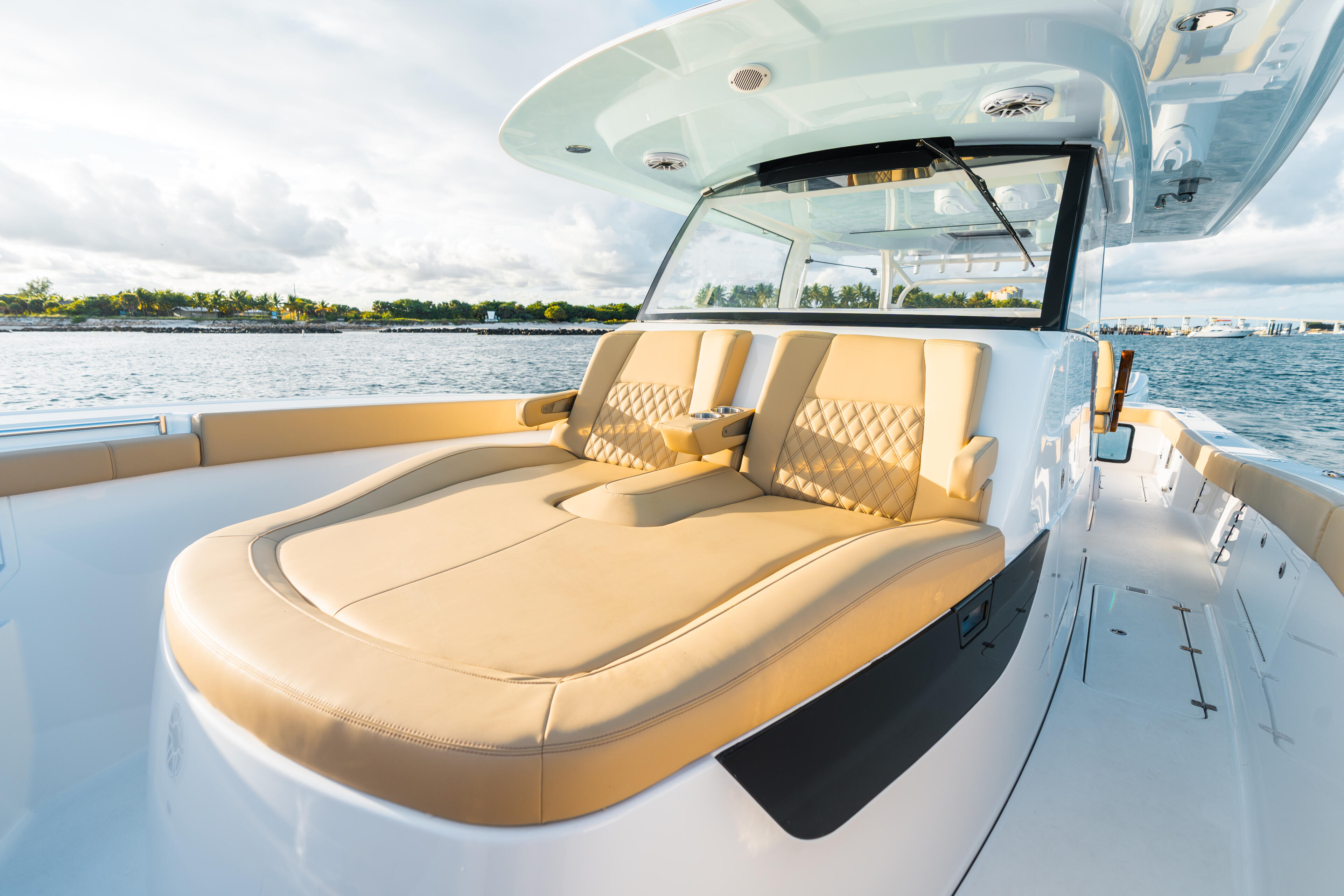 Luxury boat cockpit with tan leather seating, windshield, and hard-top canopy overlooking calm waterfront