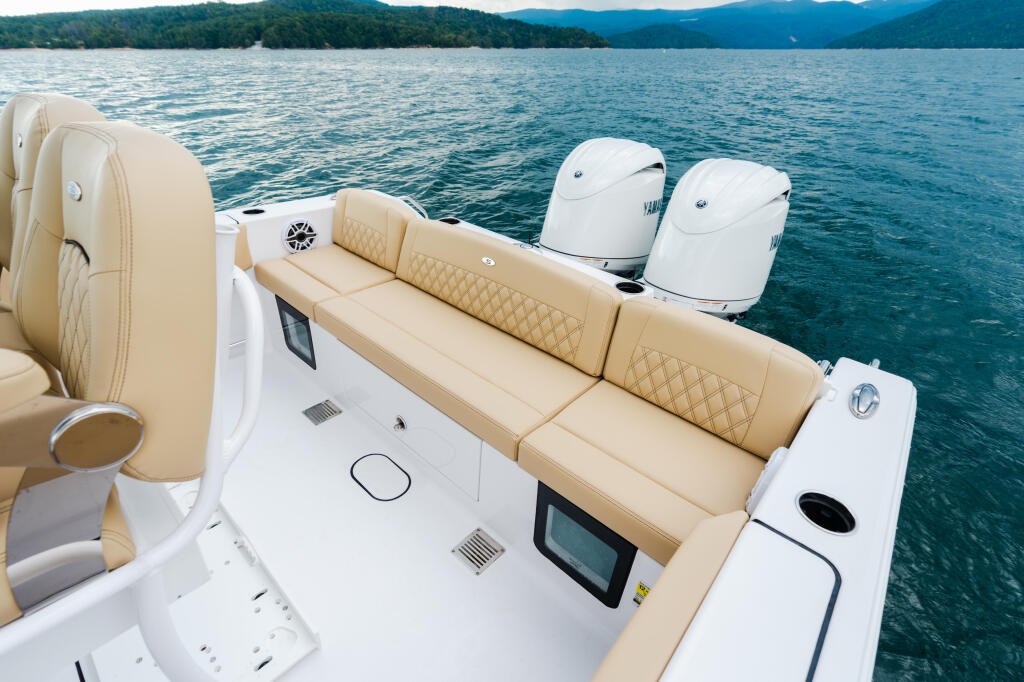Spacious boat deck with cream quilted seating, dual outboard engines, and mountains across calm water