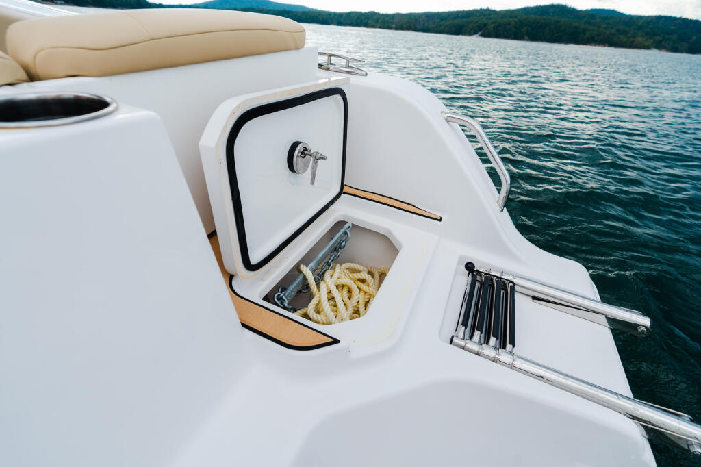Open livewell with coiled rope on a boat's deck overlooking a forested lake