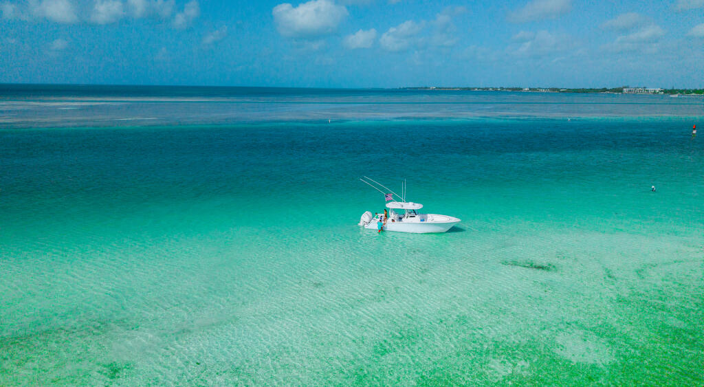 White center console boat anchored in crystal-clear turquoise water at a shallow sandbar