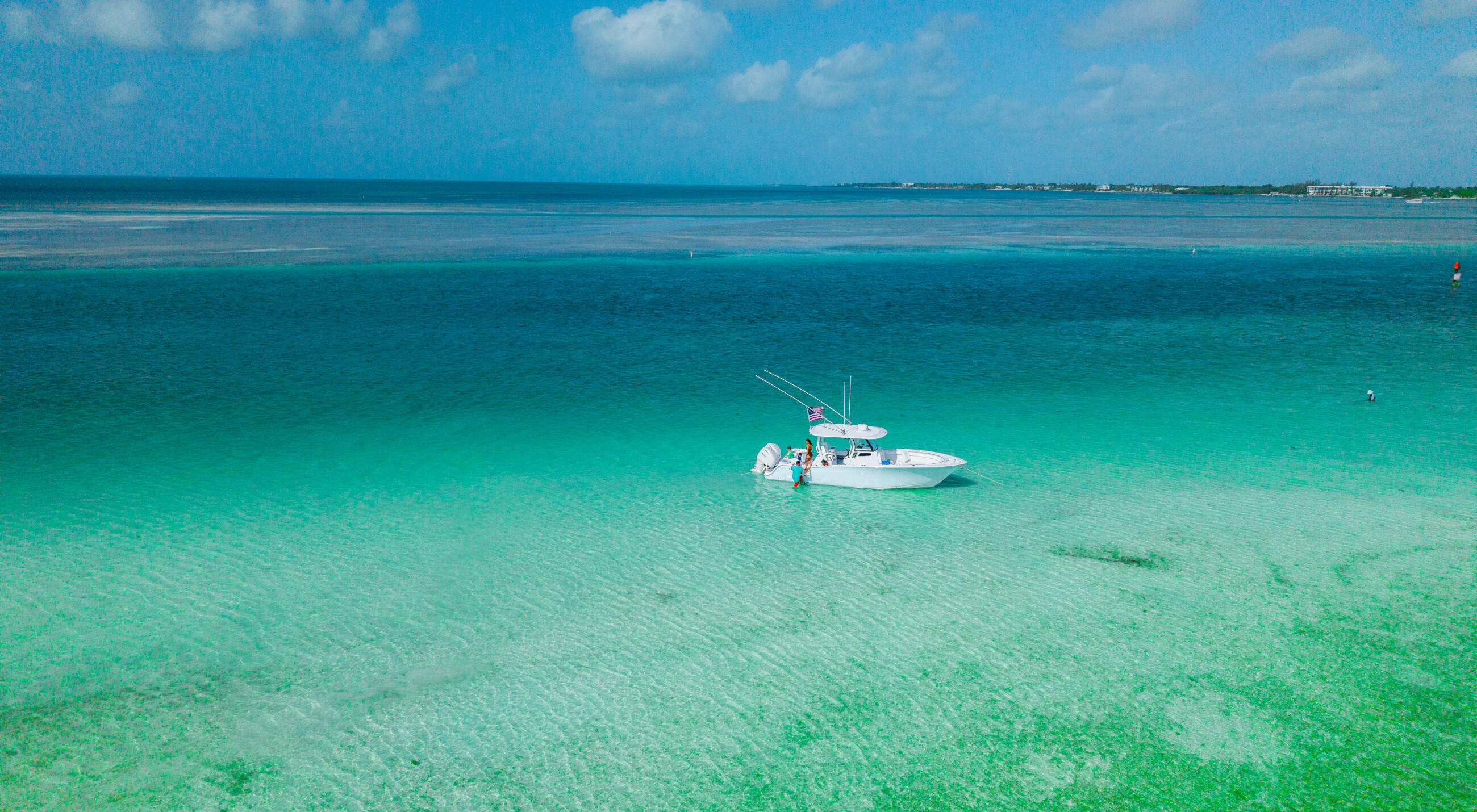 White center console boat anchored in crystal-clear turquoise water at a shallow sandbar