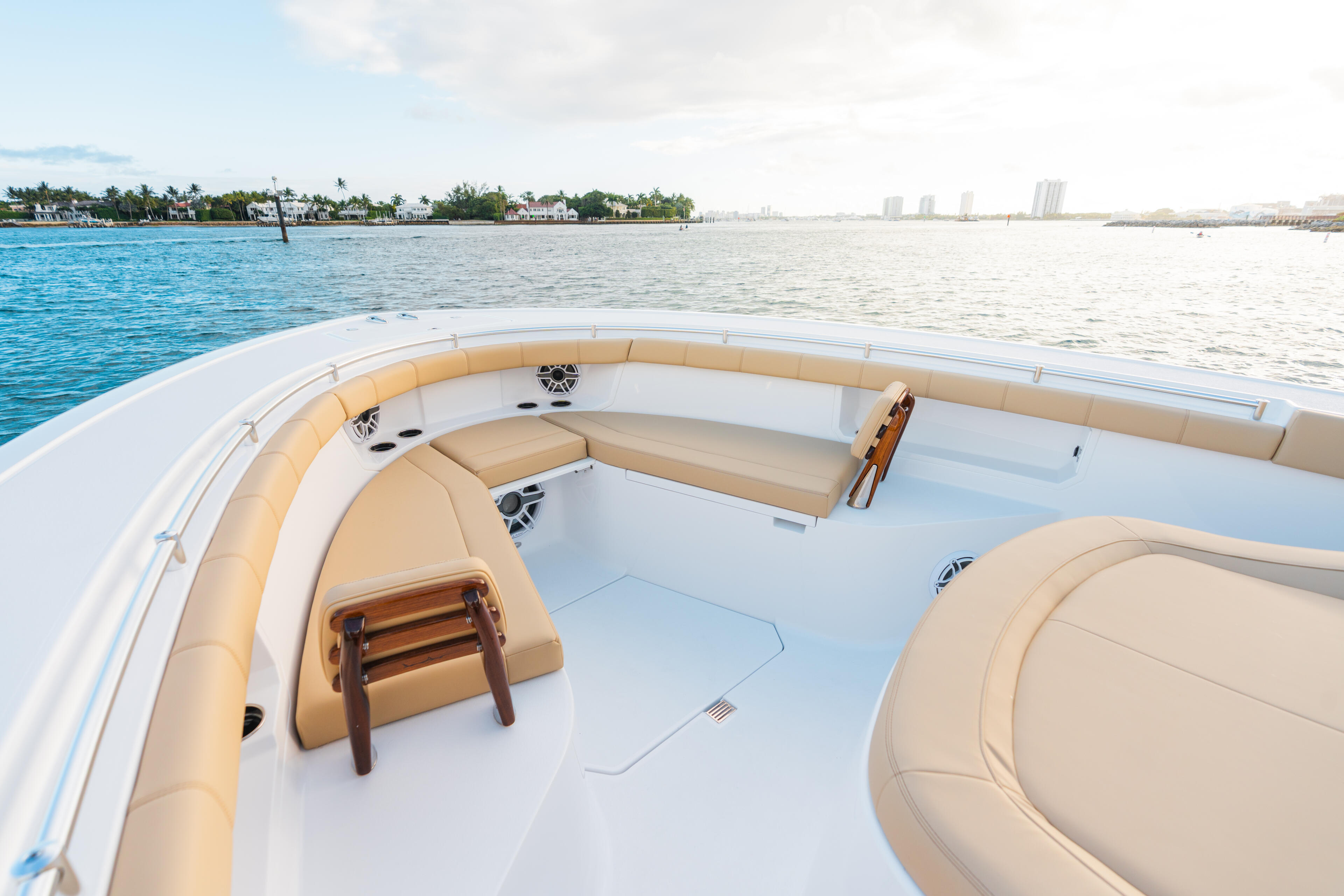 Spacious bow seating area with tan cushioned wraparound seats and wooden steering wheel on white center console boat