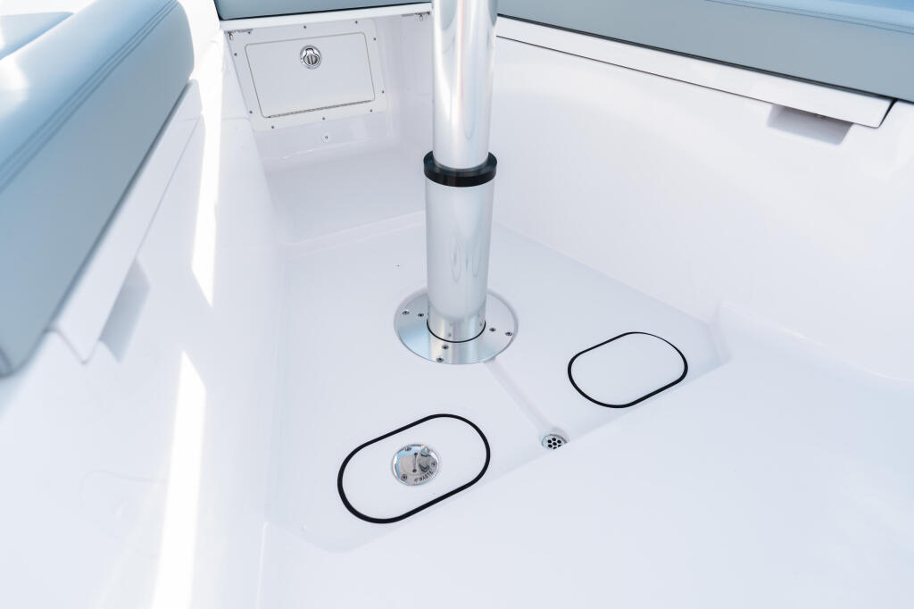 Clean white boat deck with center console, storage hatches, and deck drains in bright sunlight