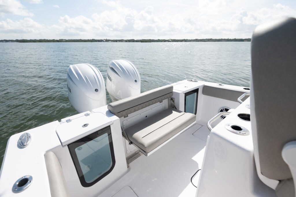 Rear bench seating with cushions and storage compartment on center console boat with dual outboard engines visible