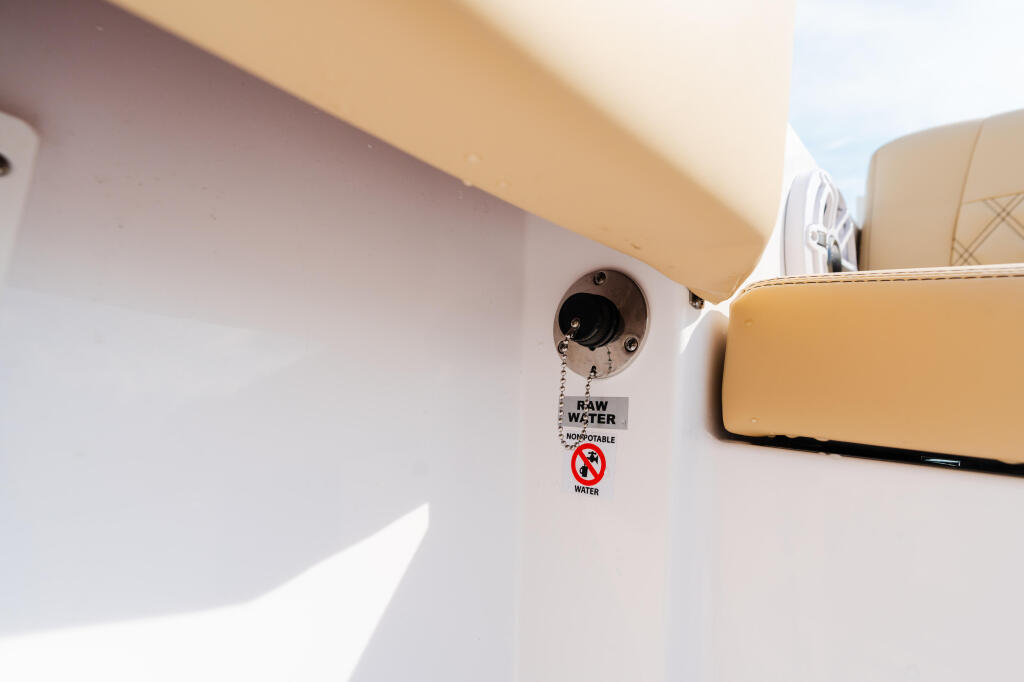 Raw water inlet with warning tag on boat cabin wall next to tan upholstered seating