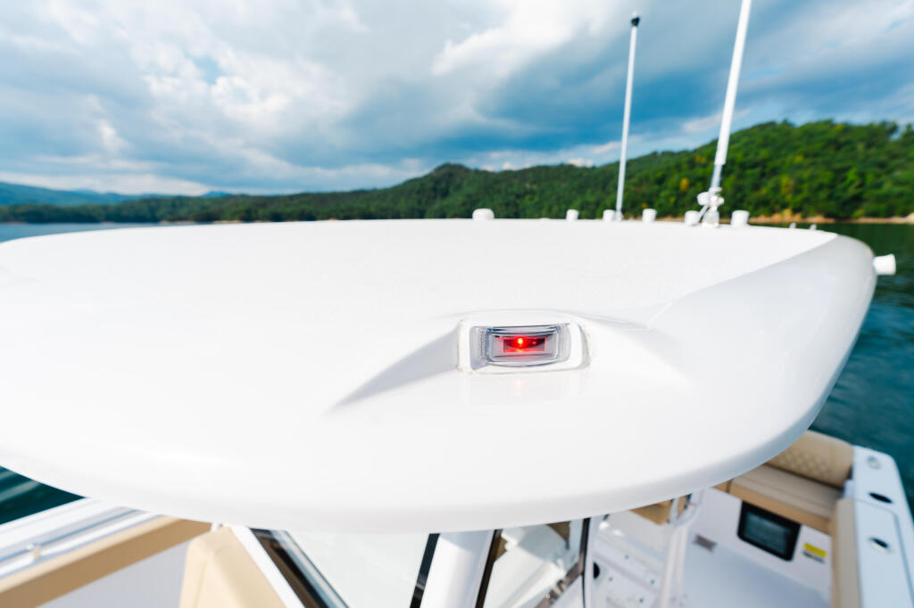 White hardtop boat with navigation light anchored on calm lake near forested shoreline