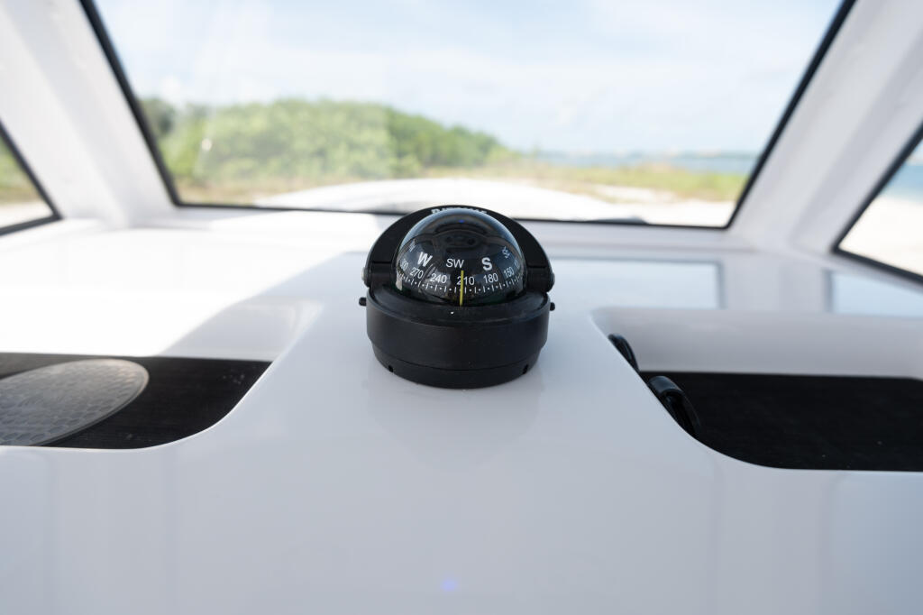 Compass mounted on white center console dashboard with windshield and sandbar view