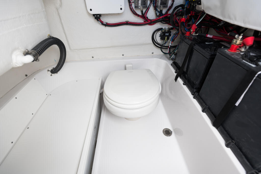 Boat cabin interior showing white head/toilet with electrical systems and battery storage compartments