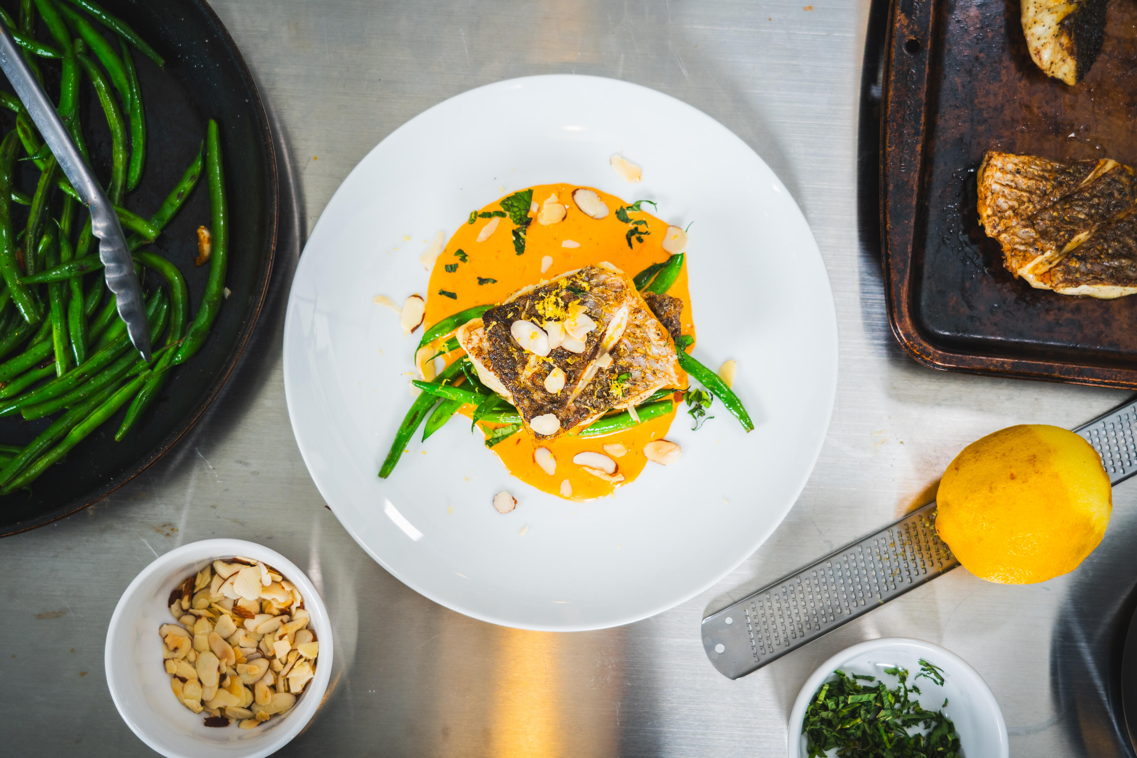 Seared redfish fillet plated with sautéed green beans and yellow pepper coulis, garnished with sliced almonds